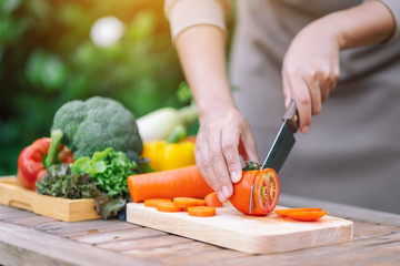 Closeup image of a woman cutting and chopping tomato by knife on wooden board