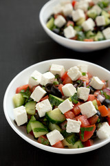 Homemade Shepherd's salad with cucumbers, parsley and feta in white bowls on a black surface, low angle view. Selective focus.
