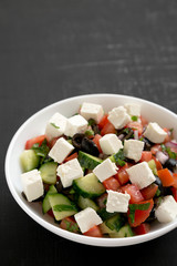 Homemade Shepherd's salad with cucumbers, parsley and feta in a white bowl on a black background, low angle view. Copy space.