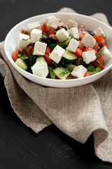 Homemade Shepherds salad with cucumbers, parsley and feta in a white bowl on a black surface, side view. Closeup.