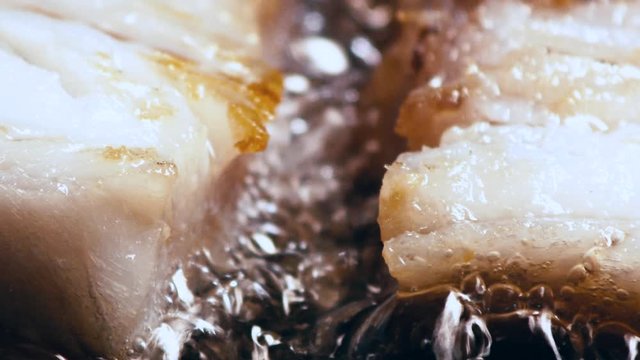 Golden fish filet cooks in sizzling oil, extreme close up.. 