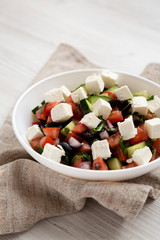 Homemade Shepards salad with cucumbers, parsley and feta in a white bowl on a white wooden surface, side view. Closeup.