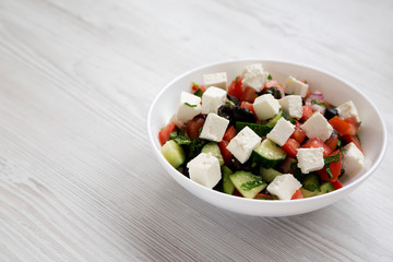Homemade Shepards salad with cucumbers, parsley and feta in a white bowl on a white wooden surface,...