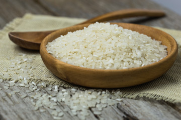 raw white rice (Thai Jasmine rice) in brown bowl and and ear of rice or unmilled rice on wooden background