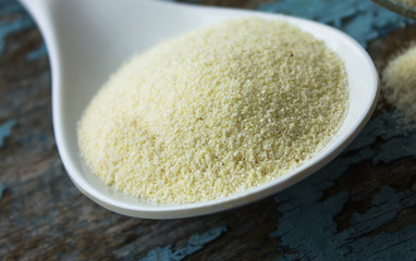 Dry semolina durum flour in a pink bowl over white wooden surface, top view.