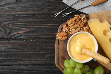 Flat lay composition with pot of tasty cheese fondue on black wooden table, space for text