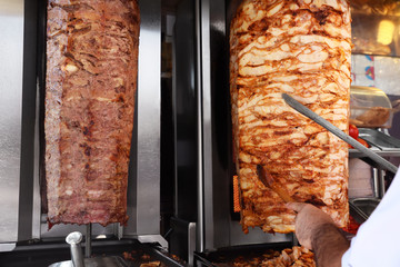 Man cutting meat from vertical rotisserie, closeup view