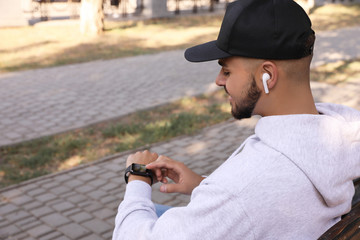 Young man with wireless headphones and smartwatch listening to music in park. Space for text