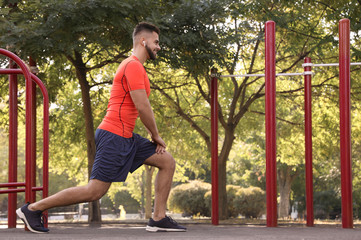 Fototapeta premium Young man with wireless headphones listening to music while exercising on sports ground. Space for text
