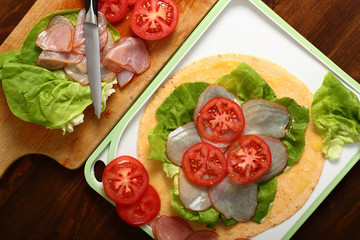 Making wrap tortilla sandwich with ham, tomato, lettuce.