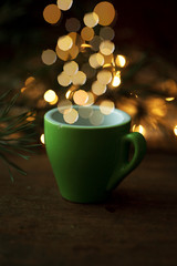 Obraz premium Coffee cup over Christmas lights bokeh in home on wooden table with tree. 