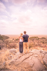 Young couple at view point looking to the bush savannah of Serengeti at sunset, Tanzania - Safari in Africa - obrazy, fototapety, plakaty