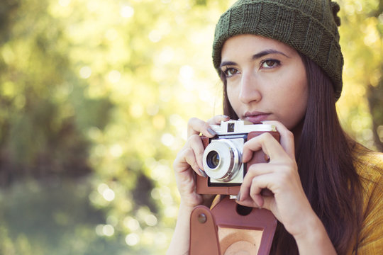 female photographer with fashionable vintage camera taking photos of nature in autumn outdoors. creative artistic woman enjoying photography.