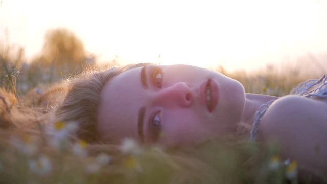 Beautiful girl lying on the meadow and dreaming. Wonderful girl with a lovely look and natural make up looking at camera. Close up slow motion footage