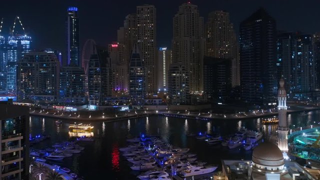 Yachts in Dubai Marina flanked by the Al Rahim Mosque with parking and residential towers and skyscrapers aerial night view. Modern high rise skyline with boats and wooden dhows