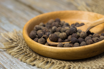 Black peppercorns in a small white bowl over stone background.