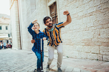 Happy father spending time with little son riding scooter.