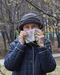 a woman with a pollen allergy covers her face with a white disposable tissue