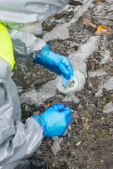 scientist in protective uniform and gloves, collects plant materials from the river in a Petri dish