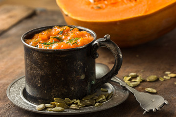 Pumpkin soup and organic pumpkins on rustic wooden table. Seasonal autumn food - Spicy pumpkin soup with thyme and pumpkin seeds.