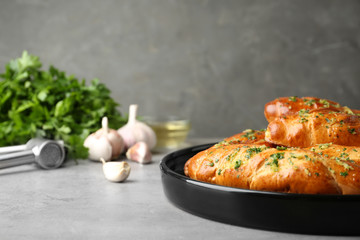 Plate of bread loaves with garlic and herbs on light table against grey background. Space for text