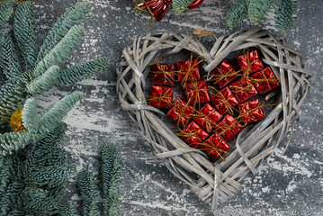 Christmas composition. Christmas gift red boxes in a wicker basket in the shape of a heart, fir branches on a gray aged background, flatlay