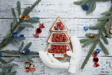 lots of little red gift boxes in the shape of a Christmas tree on a white wooden background. White knitted mittens. Fir branches on the edge of the frame . The concept of Christmas composition.