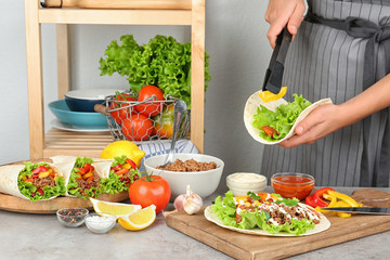 Young woman cooking delicious tortilla with meat and vegetables at table in kitchen, closeup view