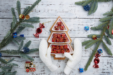 lots of little red gift boxes in the shape of a Christmas tree on a white wooden background. White knitted mittens. Fir branches on the edge of the frame . The concept of Christmas composition.