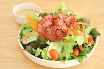 Close up fresh vegetable salad (lettuce, carrot, cucumber, tomato)  with fried bacon and roasted sesame Japanese dressing in white bowl on wooden table background
