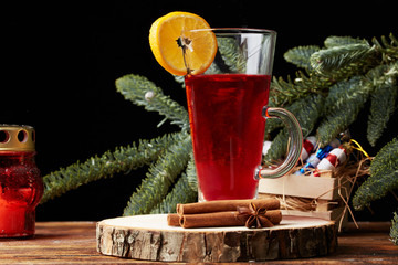Christmas mulled wine red in a glass with a stick of cinnamon and a piece of orange on the background of a tree branch. wooden background
