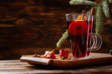 Christmas mulled wine red in a glass with a stick of cinnamon and a piece of orange on the background of a tree branch. wooden background