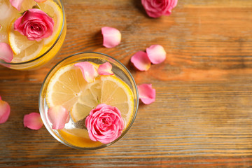 Tasty refreshing lemon drink with roses on wooden table, flat lay