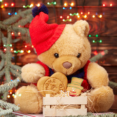 Christmas composition. Teddy bear in a red hat holding a box of homemade cookies on the background of lights Christmas garland on the branches of the Christmas tree. on the brown wooden background