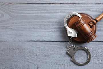Flat lay composition with handcuffs and gavel on grey wooden table, space for text. Criminal law