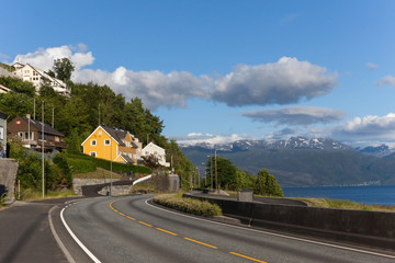Road in Norway along the fjord with a coastal village on a sunny day.