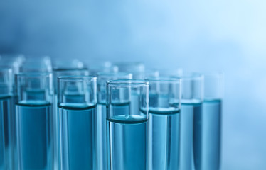 Many test tubes with liquid samples on blue background, closeup