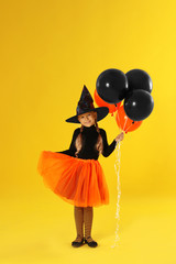 Cute little girl with balloons wearing Halloween costume on yellow background