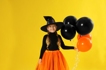 Cute little girl with balloons wearing Halloween costume on yellow background