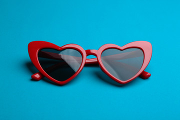 Stylish heart shaped sunglasses on blue background. Fashionable accessory