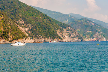 Fototapeta premium Sea yachts and boats traveling near the rocky coastline with green mountains on the background in Monterosso Al Mare, Cinque Terre