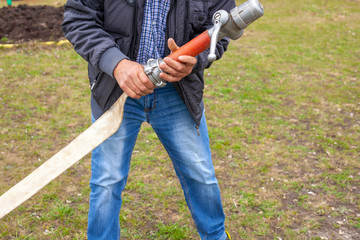 A man with a water hose to extinguish fires. A man holds a hose with water. A working gardener is preparing to water the flowerbed.