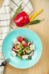 Greek salad with olives, tomatoes, feta cheese, onions in blue bowl on wooden background. Close up. Selective focus