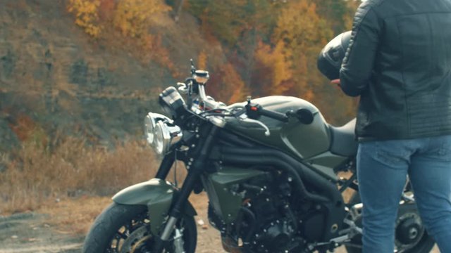 Young man with a motorcycle wears a helmet on his head. Close up slow motion footage. 4k.