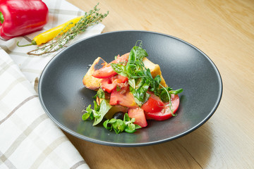 Grilled cheese salad with lettuce, cherry tomatoes in a black bowl on wooden background. Selective focus, c;ose up