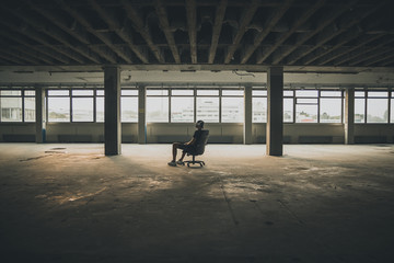 Man sitting in front of a large window in an empty hall of an abandoned building