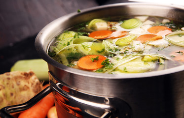 Broth with carrots, onions various fresh vegetables in a pot - colorful fresh clear spring soup. Rural kitchen scenery vegetarian broth - obrazy, fototapety, plakaty