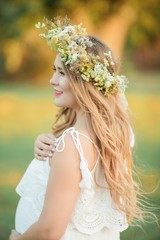 Obraz premium Portrait of a pregnant woman in the sun. Young beautiful pregnant woman with a wreath on her head in the field. Motherhood. Warm autumn.
