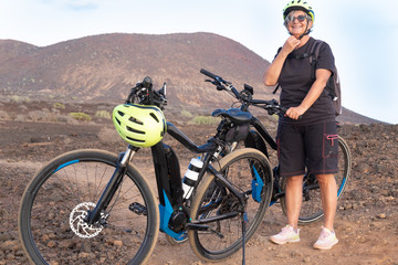 The senior woman checks the yellow helmet before starting with bicycl. Outdoor in mountain. Go with electric bicycle with battery and motor can help in the most difficult passages. A healthy lifestyle