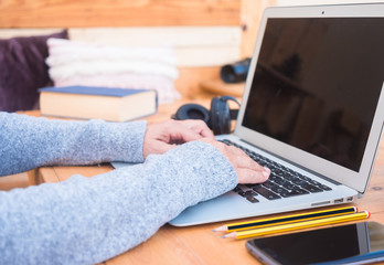 Hands of senior woman working on laptop. Alternative outdoor office. Cellphone and headphones close to her. Background and table made by recycled wood